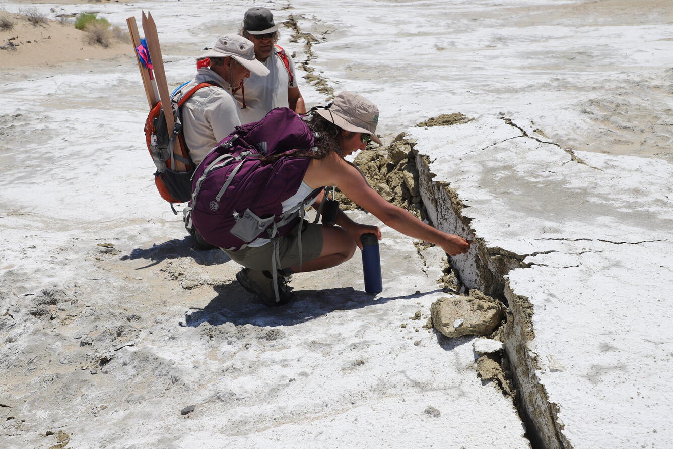A woman and two men inspect and measure a large crack in the earth's surface
