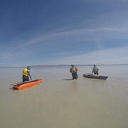 researchers wading in the lake with boats full of gear in tow behind them
