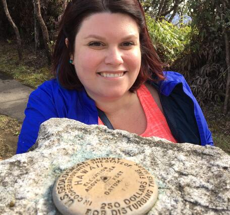 Woman standing behind USGS benchmark on rock in Hawaii