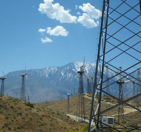 Tall windmills on a semi-arid landscape with snow-covered mountains in the background